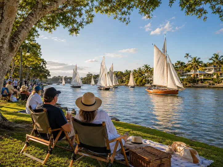 Visitors sitting by the Noosa River watching classic sailboats during the Noosa Gaff Rig Regatta in Noosaville.