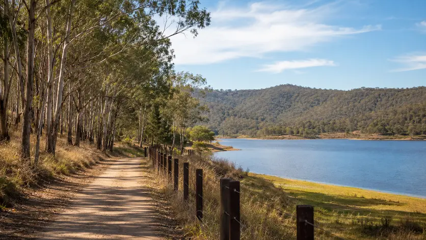 Scenic trail beside Lake Borumba in the Mary Valley, Queensland, with eucalyptus trees, calm water and forested hills.