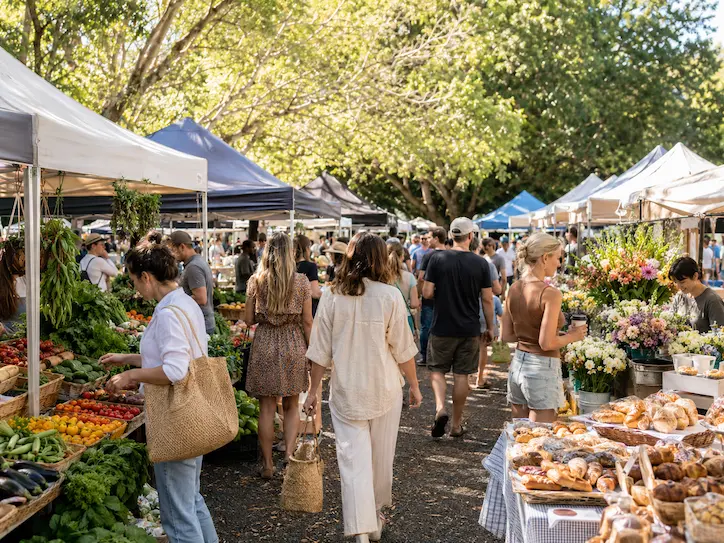 Shoppers browsing fresh produce, flowers and baked goods at a lively outdoor market near Noosa