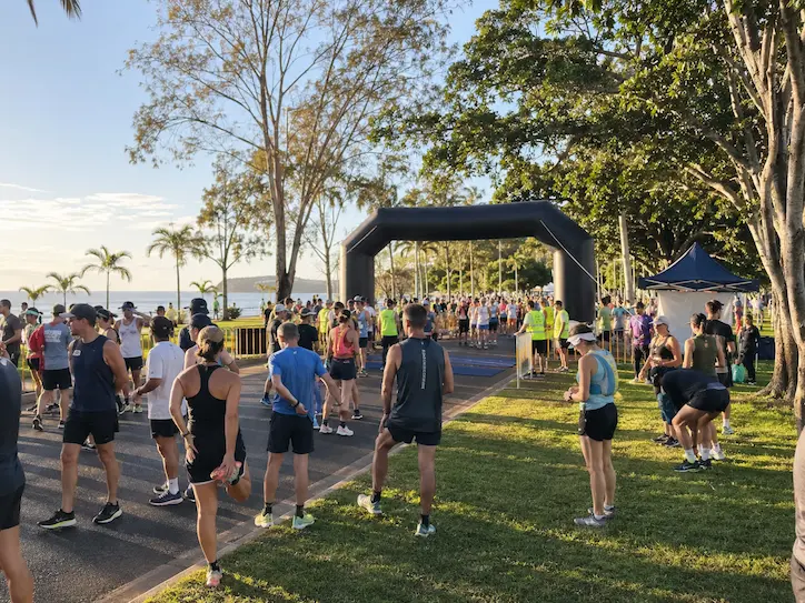 Runners gathering near a race arch and event area in Noosa before the start of a marathon weekend event.