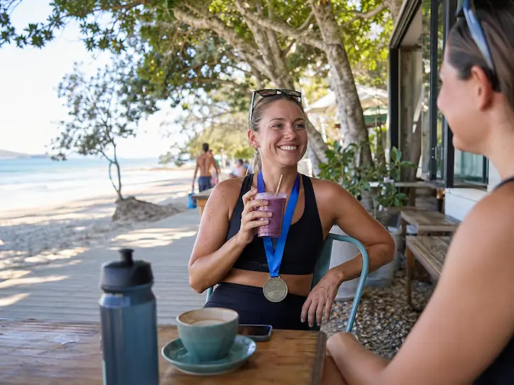 Runner wearing a medal and relaxing at a beachside cafe in Noosa after the race.