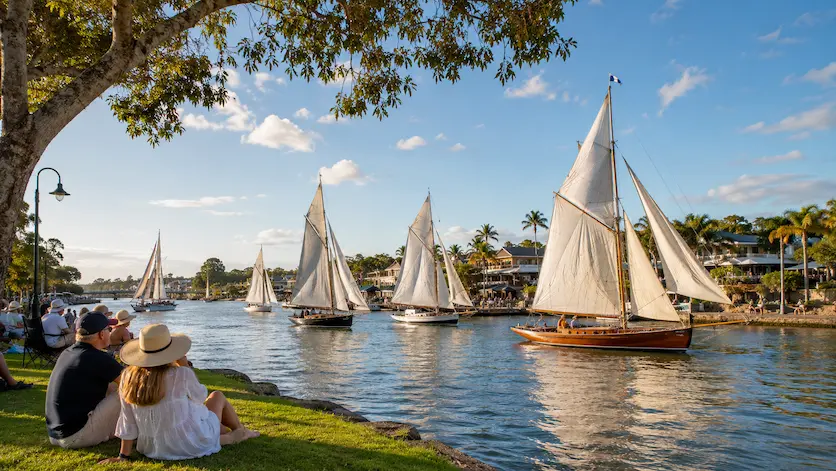 Classic gaff-rigged sailboats sailing on the Noosa River as spectators relax along the Noosaville foreshore during the Noosa Gaff Rig Regatta.